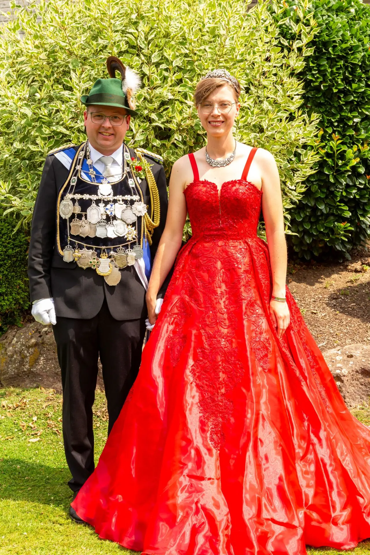 Ein Königspaar in festlicher Kleidung, bestehend aus einem Mann in Anzug und einer Frau in rotem Kleid.